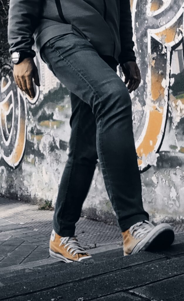 Fotografía callejera de las piernas de un hombre subiendo unas escaleras. El color del calzado, un color mostaza amarillo, coincide con los colores del graffiti que hay en la pared.